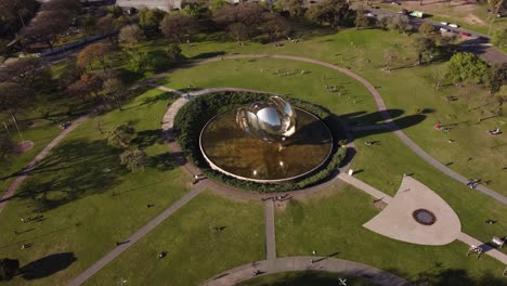 Toma-De-órbita-Aérea-Del-Parque-Floralis-Generica-Y-Mucha-Gente-Relajante-En-El-Campo-De-Hierba-Durante-La-Puesta-De-Sol---Buenos-Aires,-Argentina