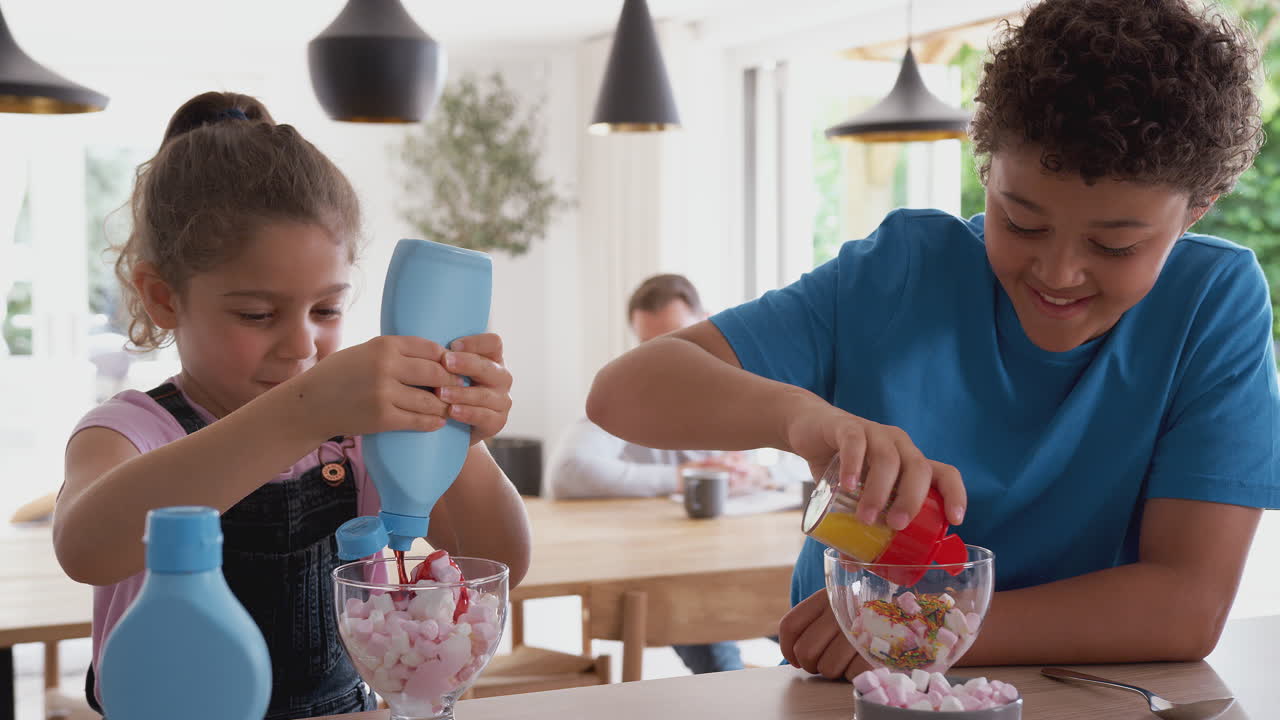 niños en la cocina en casa añadiendo salpicaduras y salsa al postre de helado