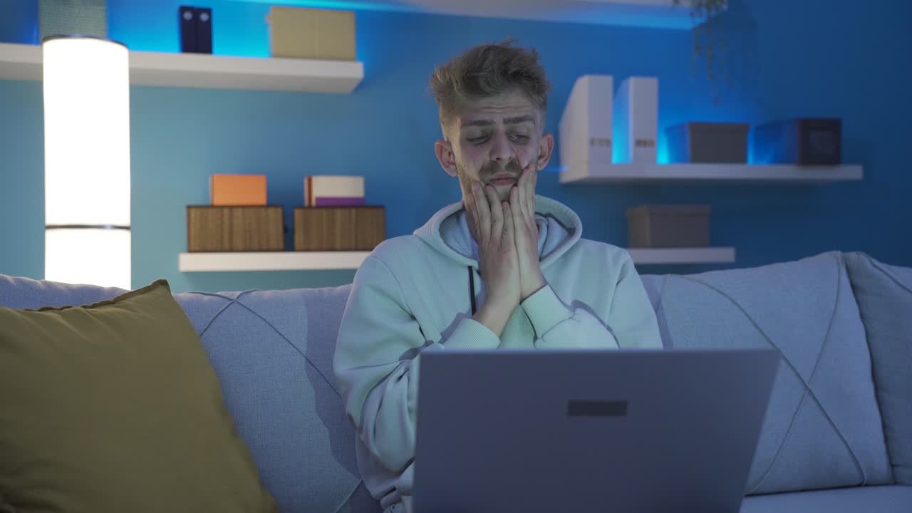 Worried and insecure discouraged young man using laptop at home