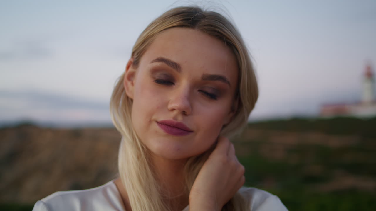 Rolig pige rører ved håret, vertikalt portræt. Blond kvinde poserer i naturen.