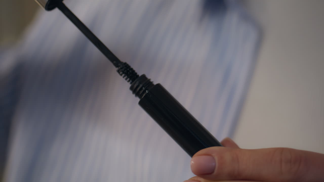 Hands open mascara tube closeup. Makeup artist holding black brush for eyelashes
