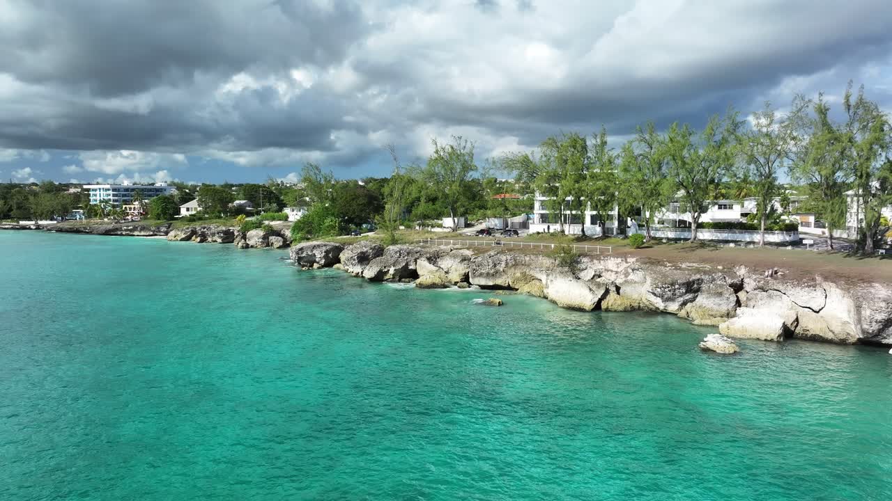 Drone shot of rocky cliffs, turquoise water, and seaside homes along the coast of Barbados