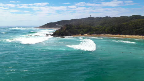 Wide-cinematic-drone-shot-of-surfers-in-the-water-and-island-in-background-at-Wategos-Beach-Australia