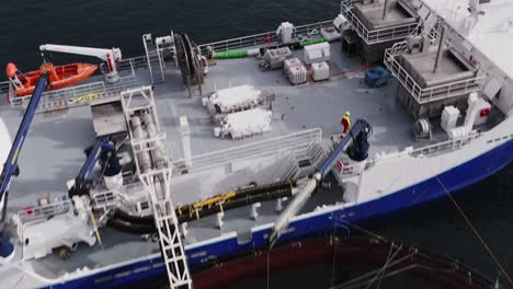 tilting drone shot of a well-boat docked at a fish cage on the hebrides