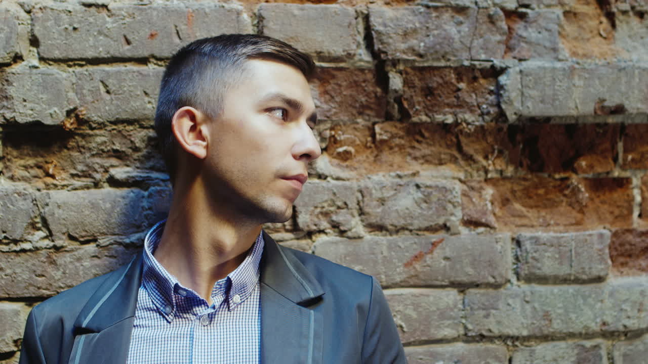 괴로워하는 젊은 사업가의 초상화는 오래된 벽돌 벽의 배경에 있어야 합니다