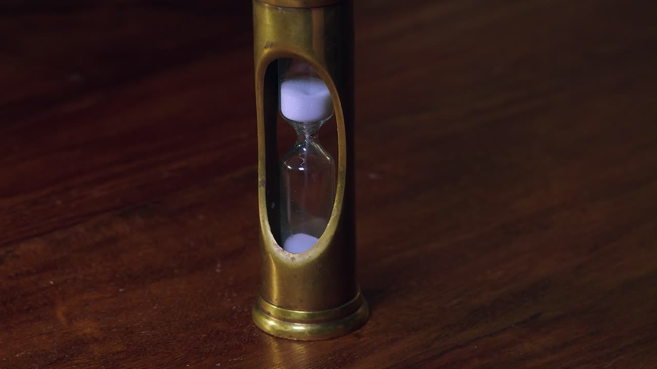 gránulos blancos caen a través del temporizador de vidrio de bronce en la mesa de madera