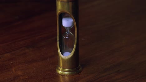 White-granules-drop-through-brass-hour-glass-timer-on-wooden-desk