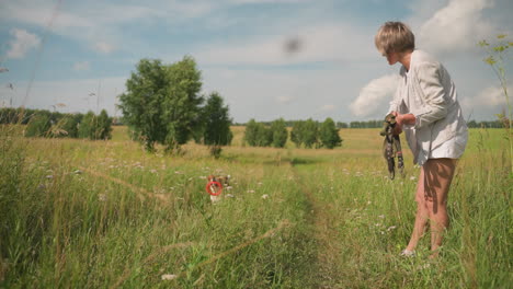 pet lover stands on grassy field holding dog leash while her dog runs back with toy in mouth, showing excitement and energy under sunny sky, outdoor fun scene captures human-animal bond