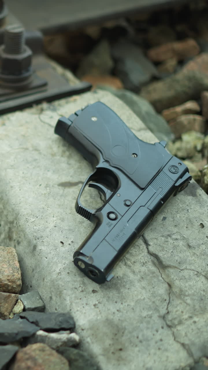 una vista cercana de una pistola colocada en la base de hormigón de una vía ferroviaria rodeada de rocas, con vista de la pierna de alguien