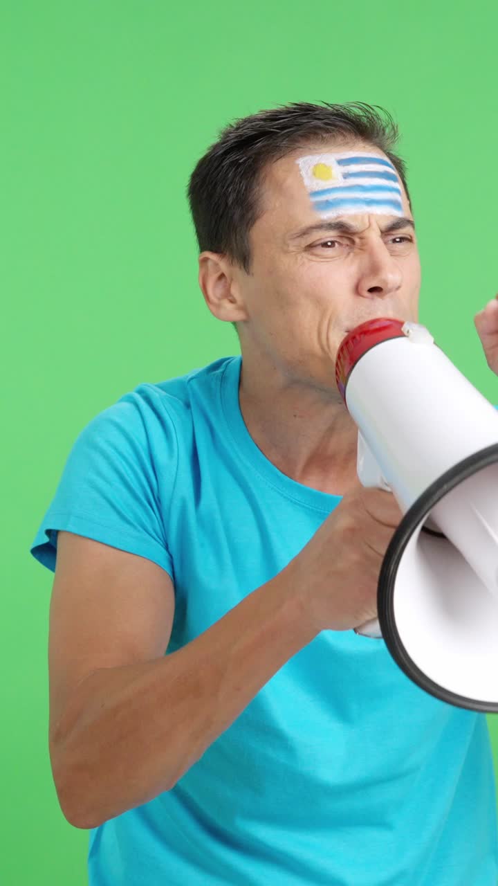 Excited man with uruguayan flag on face using a megaphone