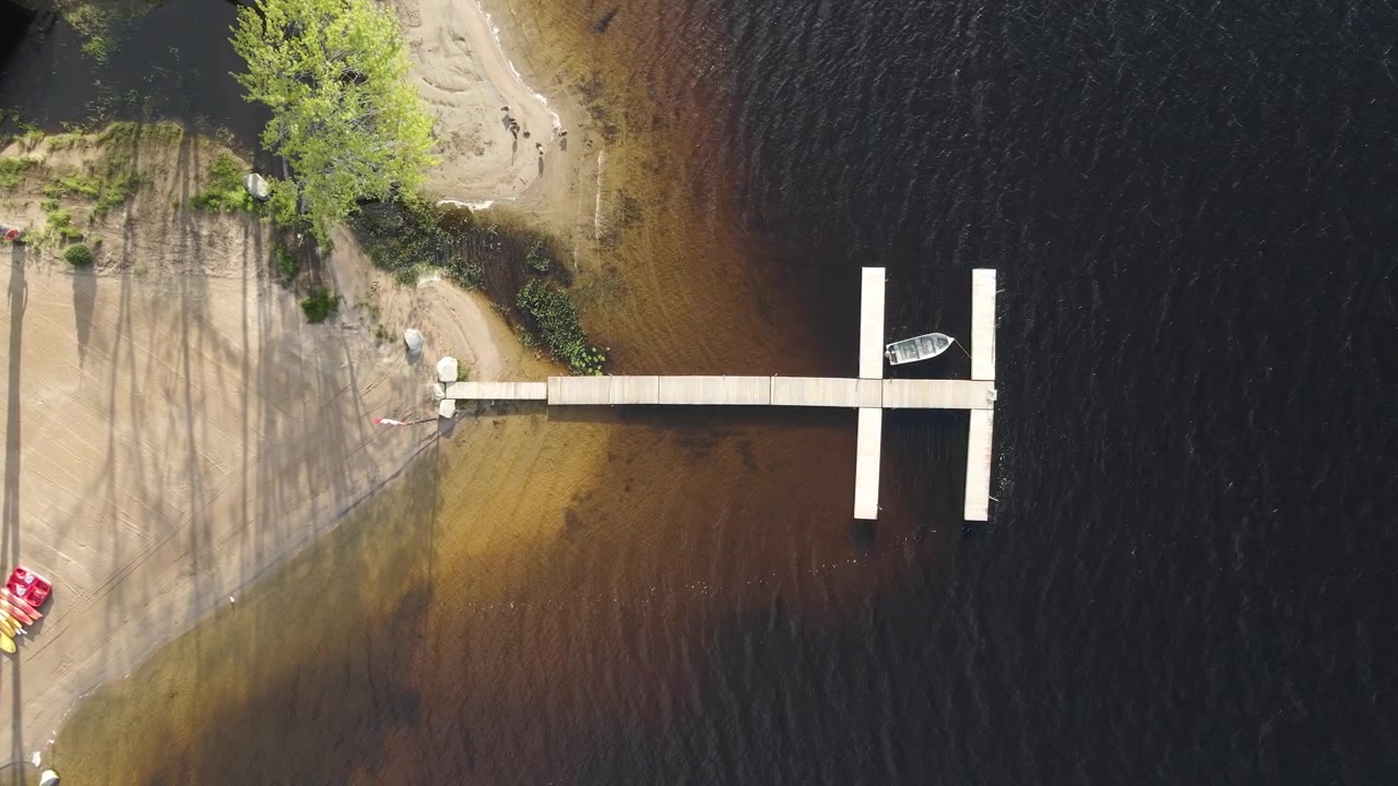 Discesa aerea su un molo sul lago con una singola barca e una spiaggia sulla riva del lago Commanda, drone