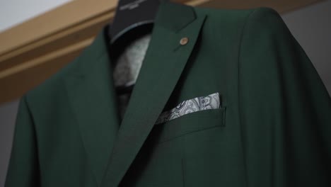 close-up of a green suit jacket with a patterned pocket square, hanging on a hanger