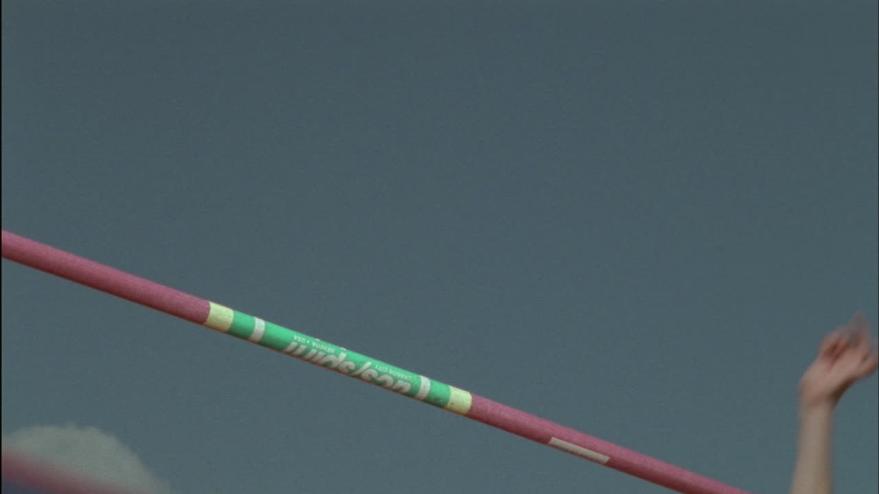 한 소녀가 막대 위로 높이뛰기를 하고 매트에 착지합니다.