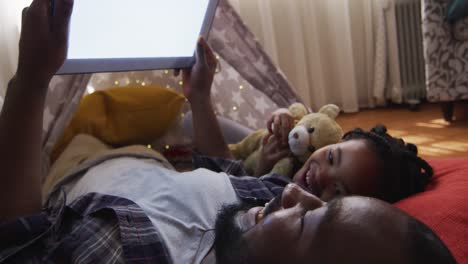 african american father and daughter lying in makeshift tent and using tablet with copy space
