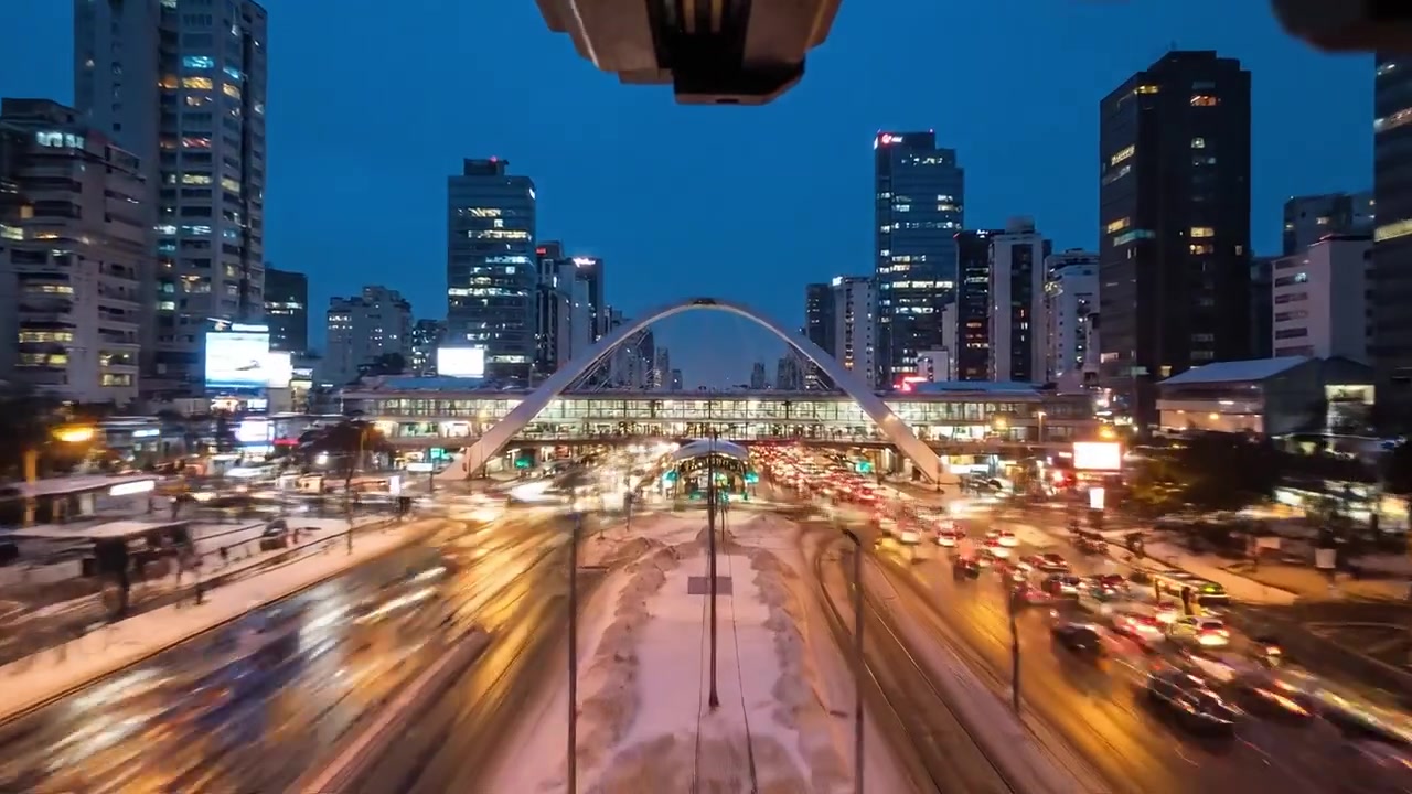 A Winter Evening in a Snowy Urban Landscape, Showcasing Illuminated Skyscrapers and Busy Traffic Under a Snowflake-Laden Sky in a Bustling Metropolis