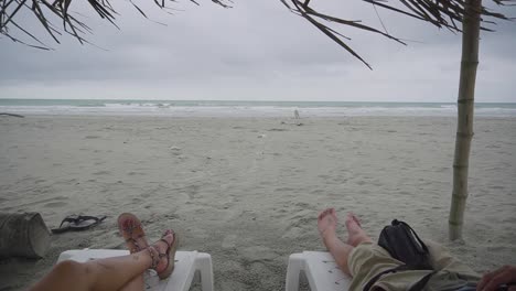 Couple-enjoys-sunbed-on-windy-and-stormy-day-on-sandy-beach-of-Ecuador