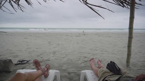 couple enjoys sunbed on windy and stormy day on sandy beach of ecuador