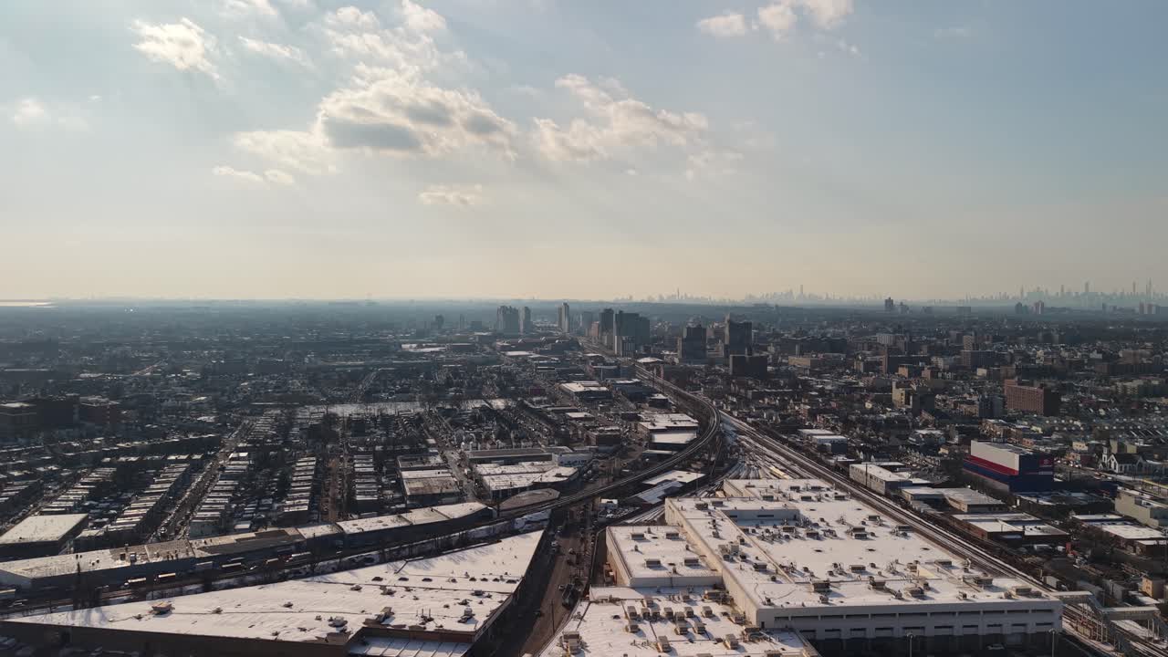 Expansive aerial view slowly revealing a vast urban and industrial area covered in snow under a bright, sunny winter sky, showcasing the city's sprawl and infrastructure with a distant skyline