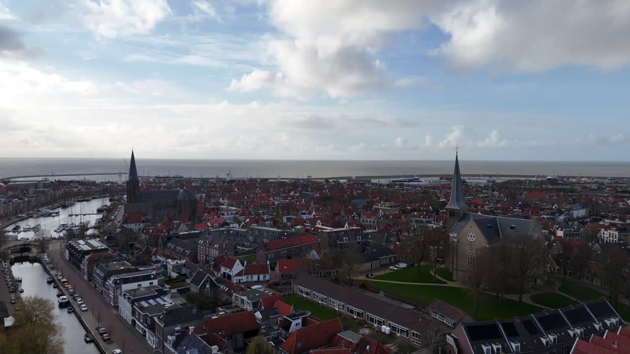 Ascesa verticale del drone sopra gli alberi del canale che rivela campanili, il porto e il Mare del Nord.
