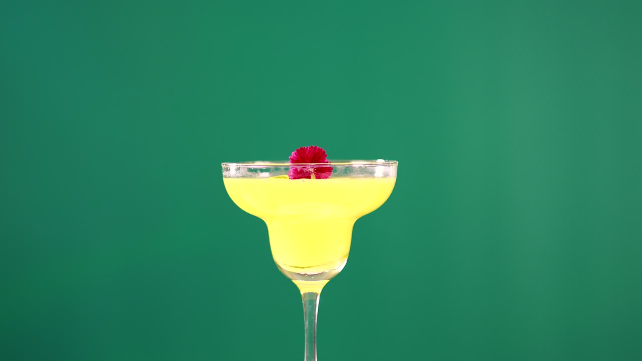 A yellow cocktail in a glass with a cherry garnish against a green screen backdrop, showcasing vibrant colors
