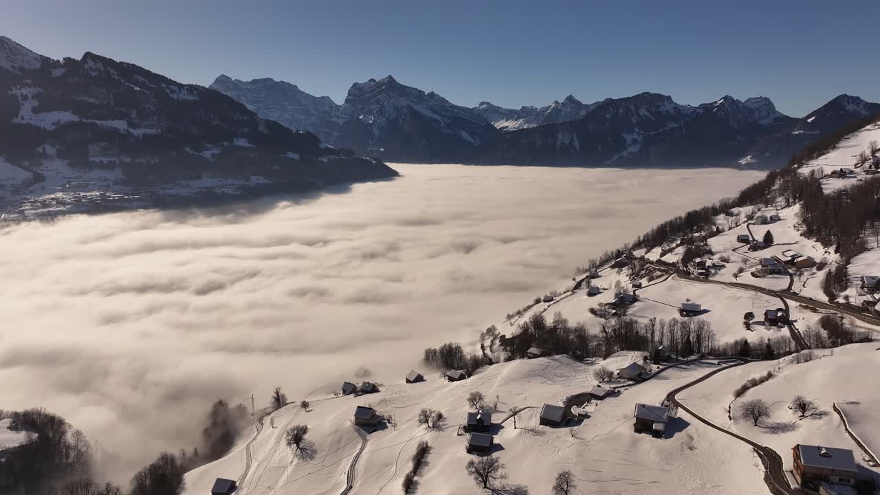 Aerial view of a breathtaking sea of fog blanketing the stunning Wallensee in Switzerland, with snow-capped mountains rising above the clouds and charming villages nestled in the winter landscape.