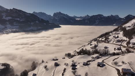aerial view of a breathtaking sea of fog blanketing the stunning wallensee in switzerland, with snow-capped mountains rising above the clouds and charming villages nestled in the winter landscape.
