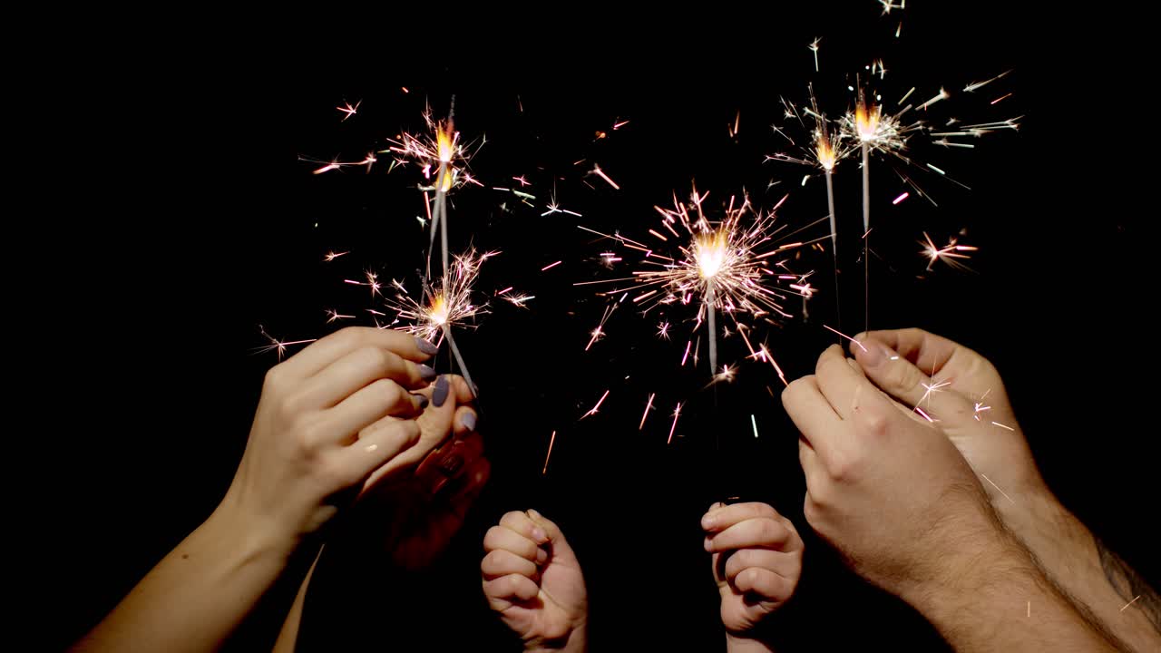 primer plano de manos sosteniendo y agitando fuego bengal quemando chispas frente a un fondo negro