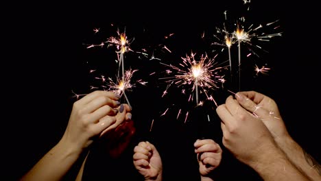 close-up of hands holding and waving bengal fire burning sparklers in front of black background