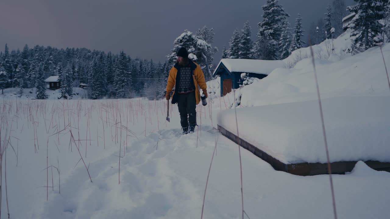 hombre con hacha y matraz de vacío caminando sobre la nieve en invierno