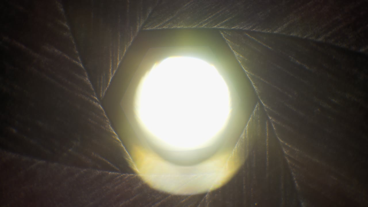 las cuchillas del diafragma se abren rápidamente con el sol brillando a través de la vieja lente de la cámara, se desvanecen a blanco