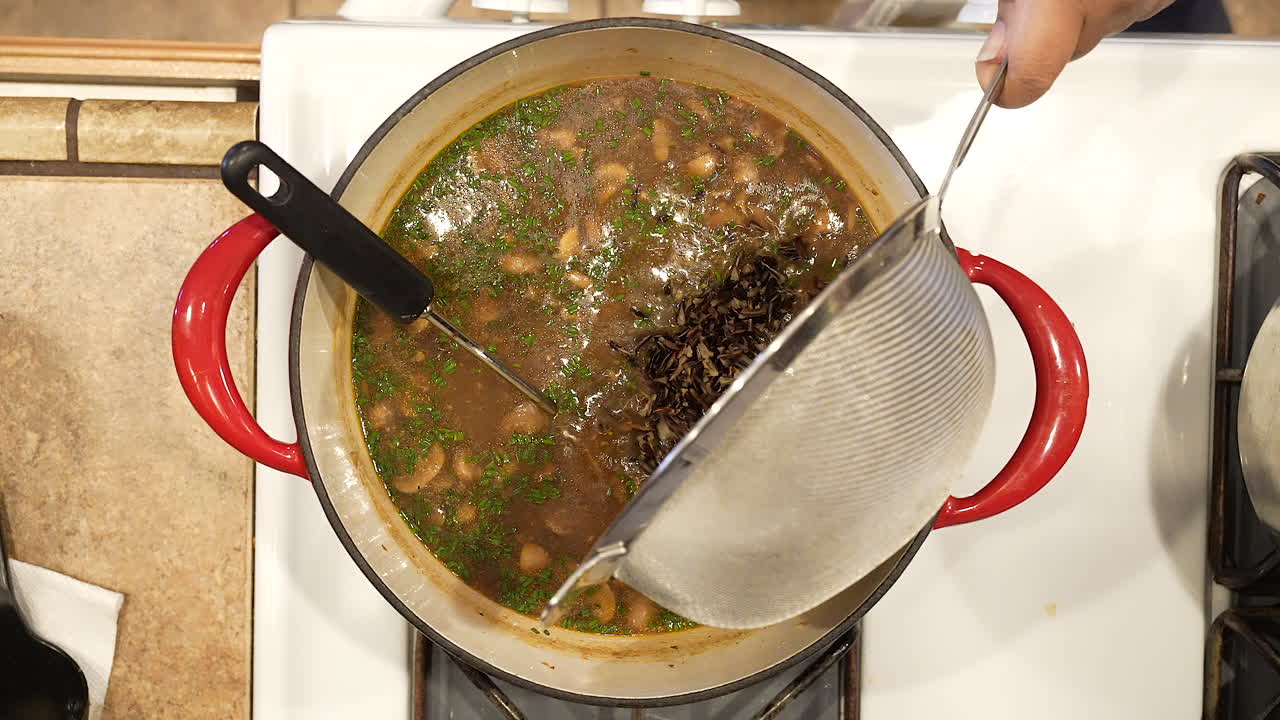 verter arroz salvaje cocido en una olla de champiñones y caldo para hacer una sabrosa sopa vegana en cámara lenta - vista aérea de la serie de arroz salvaje