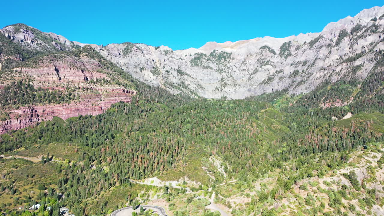공중 드론은 여름 동안 아름다운 우레이 콜로라도의 두꺼운 소나무 숲과 산봉우리 위로 550번 고속도로에서 록키 마운틴 하우스로 운전하는 자동차와 함께 날아갑니다.