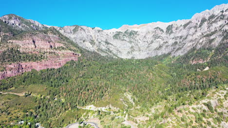 aerial drone fly over of beautiful ouray colorado thick pine tree forest and mountain peaks during summer with cars driving on highway 550 by rocky mountain houses