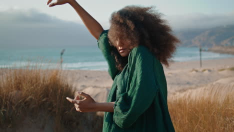 Dancer-woman-moving-hands-smoothly-standing-at-sandy-dunes-with-dry-grass.