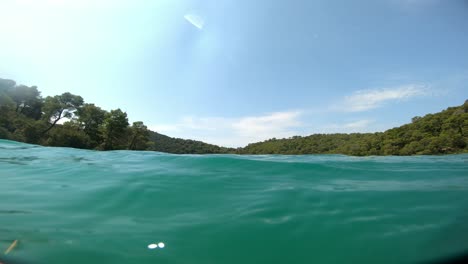 Diving-into-beautiful-turquoise-water-with-reflections-and-light-on-the-surface-and-forest-in-the-distance