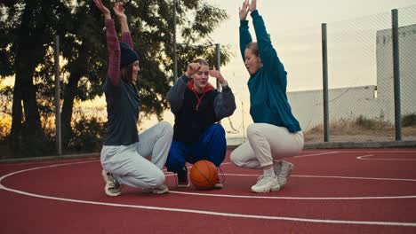 Drei-Mädchen-Falten-Beim-Morgendlichen-Basketballtraining-In-Der-Nähe-Des-Basketballballs-Ihre-Hände-Und-Heben-Sie-Als-Zeichen-Der-Einheit-In-Die-Höhe.-Dann-Beginnen-Sie-Im-Sommer-Frühmorgens-Mit-Dem-Training.