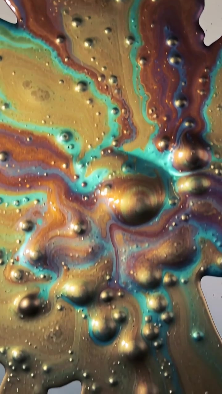 Video verticale: Goccioline che cadono e si fondono in vernice iridescente su vetro in uno studio macro per gravità.