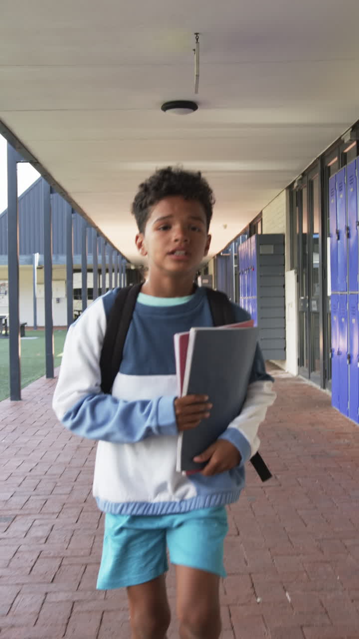 Vertical video: In school, boy holding books and walking in hallway with backpack