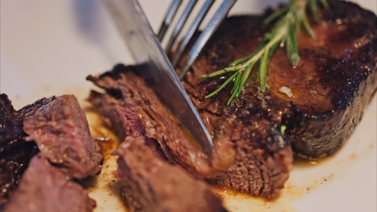 Close up of a woman cutting up a beef steak of with rosemary on a white plate at a restaurant