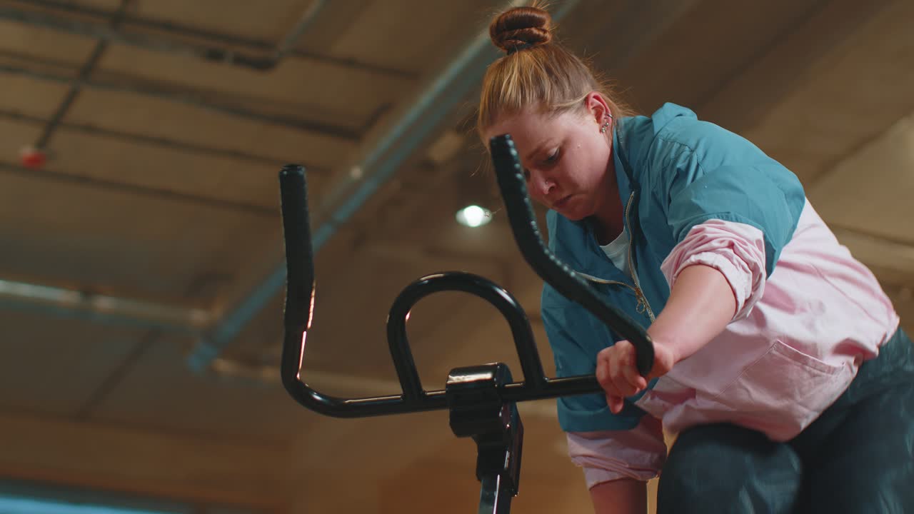 Healthy caucasian woman exercising workout on stationary cycling machine bike in gym slow motion