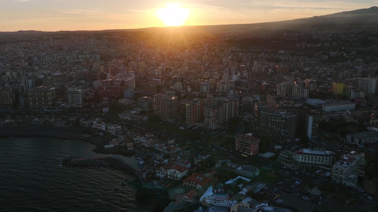 Italia Sicilia: Ripresa aerea con drone in tilt-up del paesaggio urbano di Catania e orizzonte al tramonto sulla costa