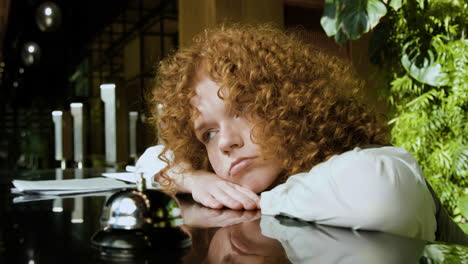 Close-up-view-of-tired-redheaded-receptionist-behind-the-counter