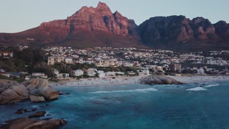 Drone-Volando-Sobre-La-Playa-De-Camps-Bay,-Revelando-Más-De-La-Zona-Costera-Durante-La-Puesta-De-Sol-En-Ciudad-Del-Cabo,-Sudáfrica