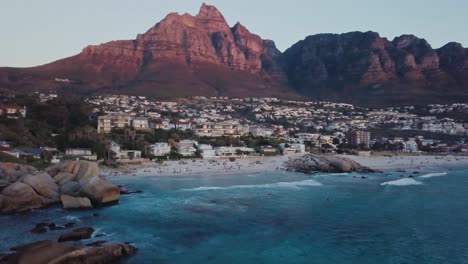 drone volando sobre camps bay beach revelando más de la zona costera durante la puesta de sol en ciudad del cabo, sudáfrica