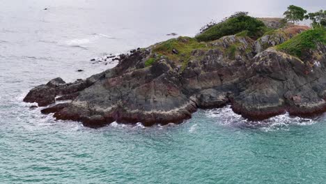 aerial footage glides over a rocky, green-topped cape meeting turquoise waters near port douglas, with steady camera movement and soft natural daylight
