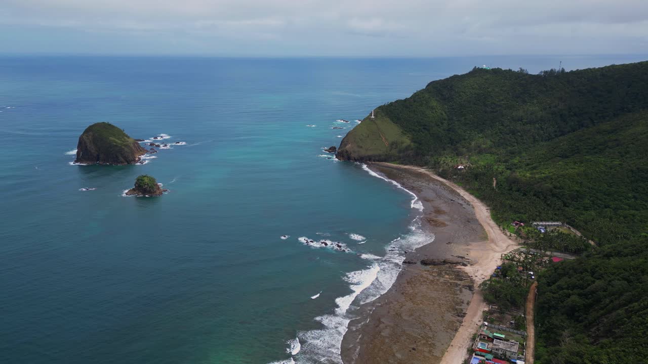 A stunning wide drone shot captures the shoreline stretching along the coast, with waves gently crashing onto the sandy beach under the open sky.