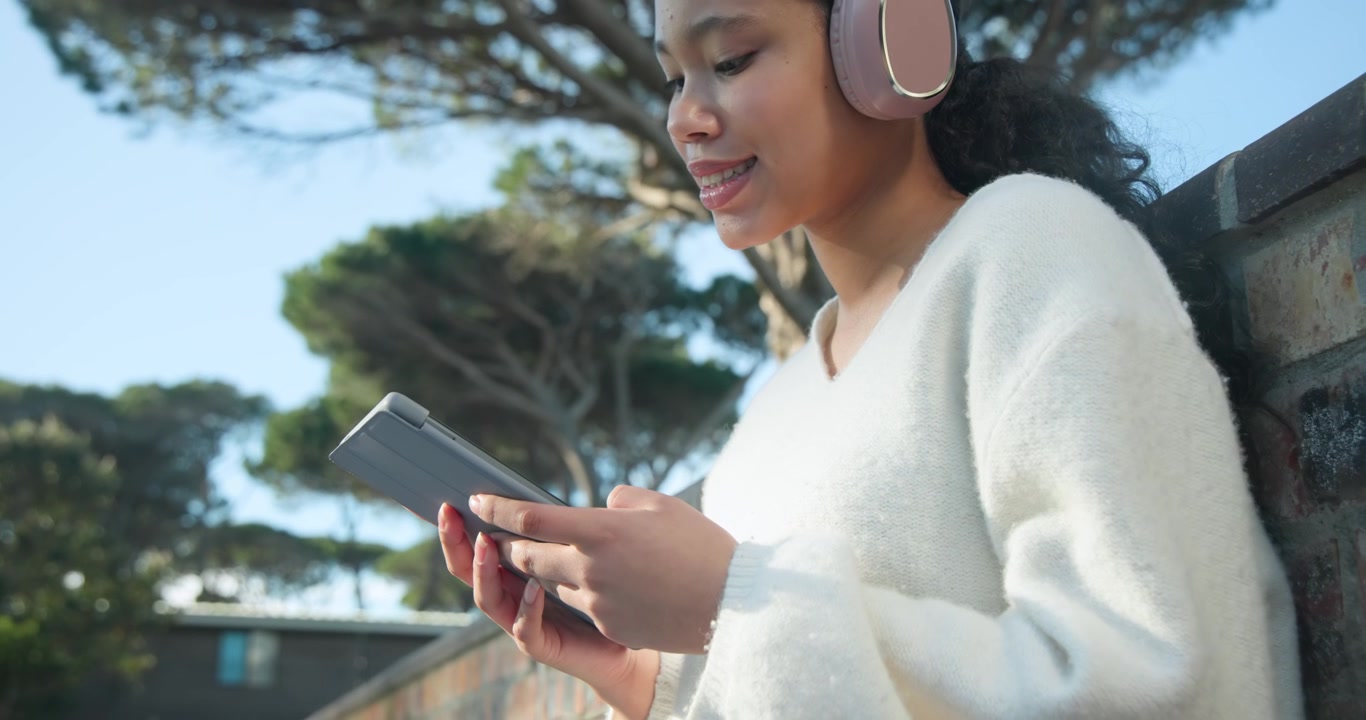 Child female sitting on park bench looking down and tapping tablet, engaging, with pink headset