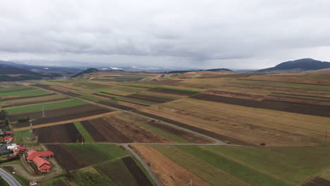 flyover above beautiful fields, farmland around sancraieni, romania. ciuc mountain range