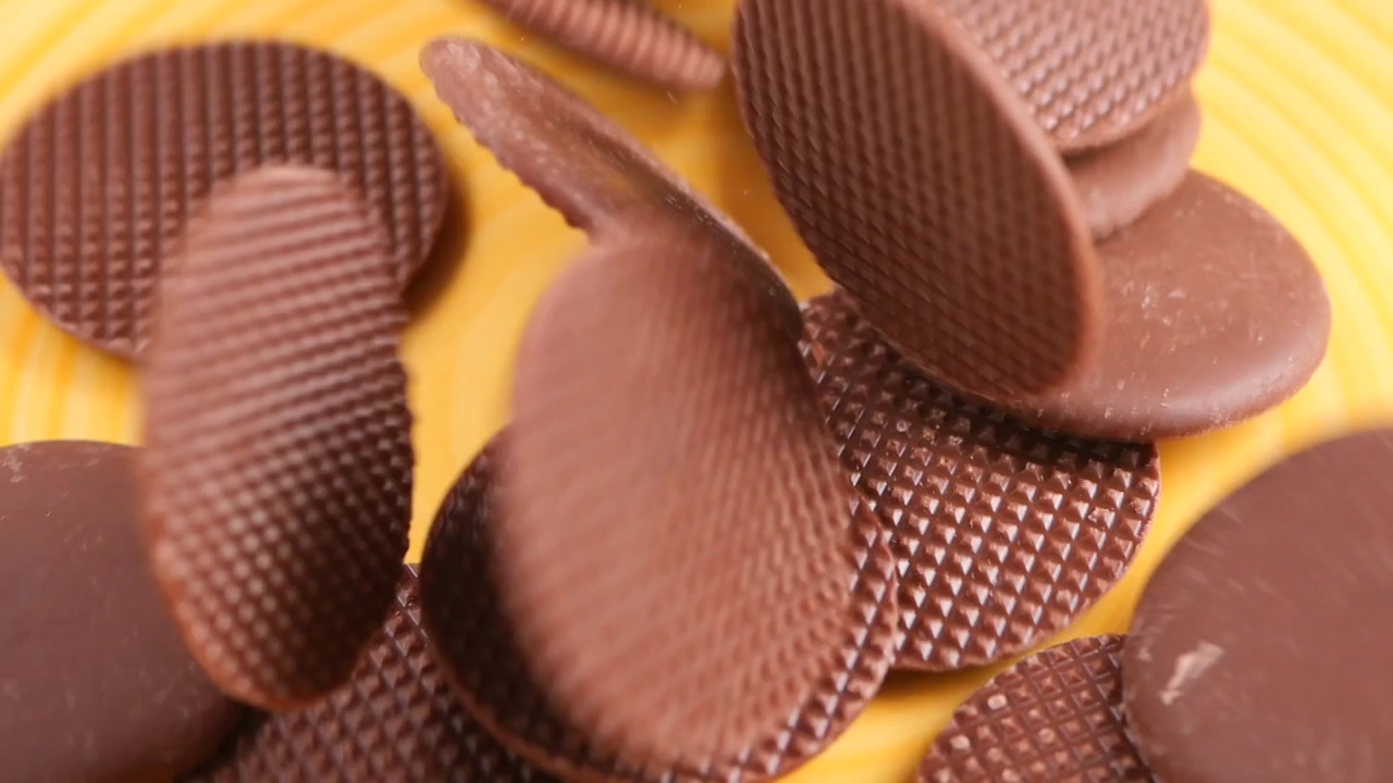 Slow Motion Chocolate Discs Falling on Yellow Plate