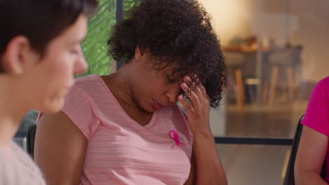 close up of upset woman wearing pink breast cancer awareness ribbon meeting and talking at therapy support group for cancer treatment patients